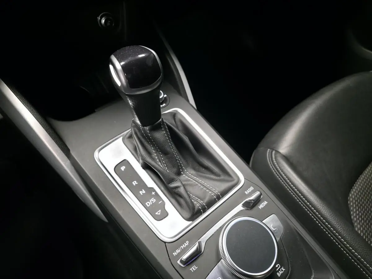 Gros plan sur la console centrale de l'Audi Q2 gris, montrant le levier de vitesse automatique et la molette de commande multimédia.