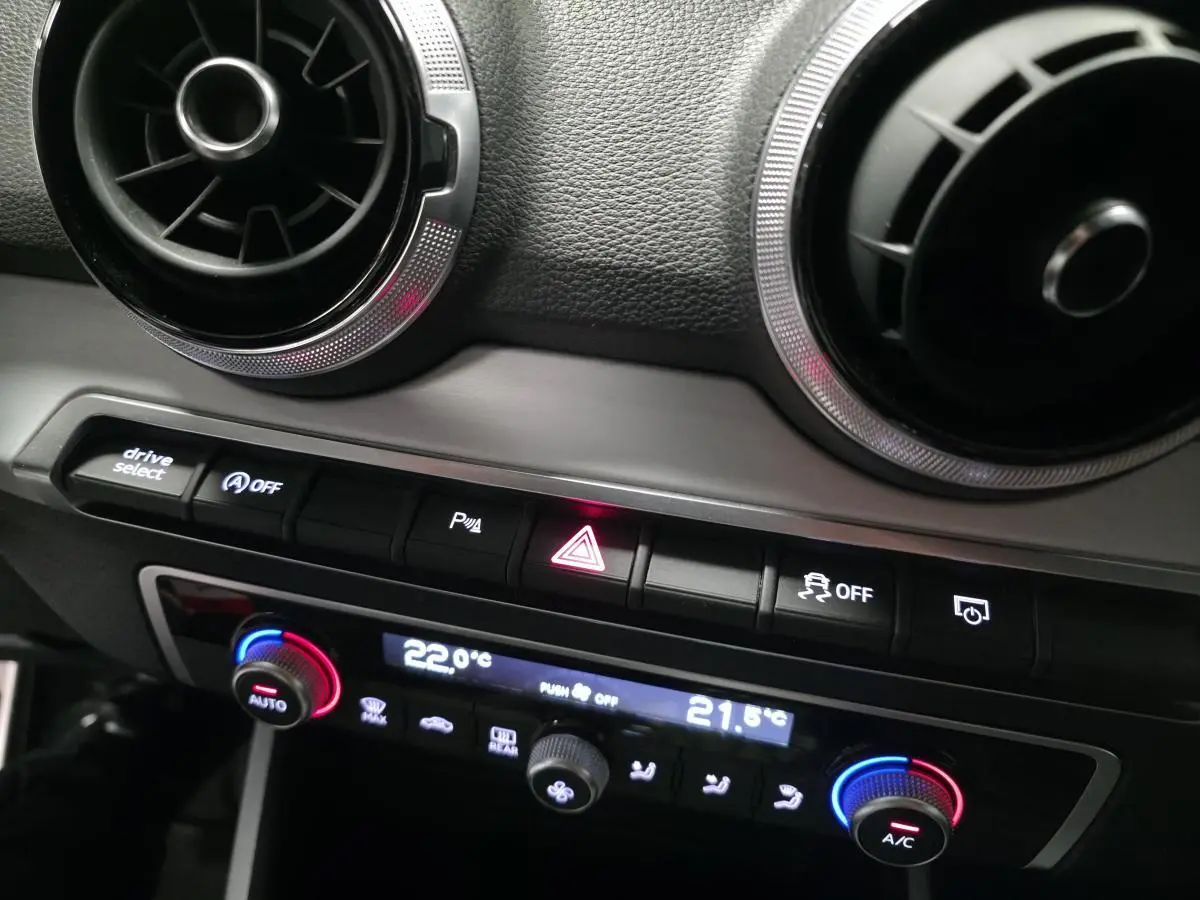 Détail de la console centrale de l'Audi Q2 2023 gris, montrant les aérateurs ronds et les commandes de climatisation automatiques.