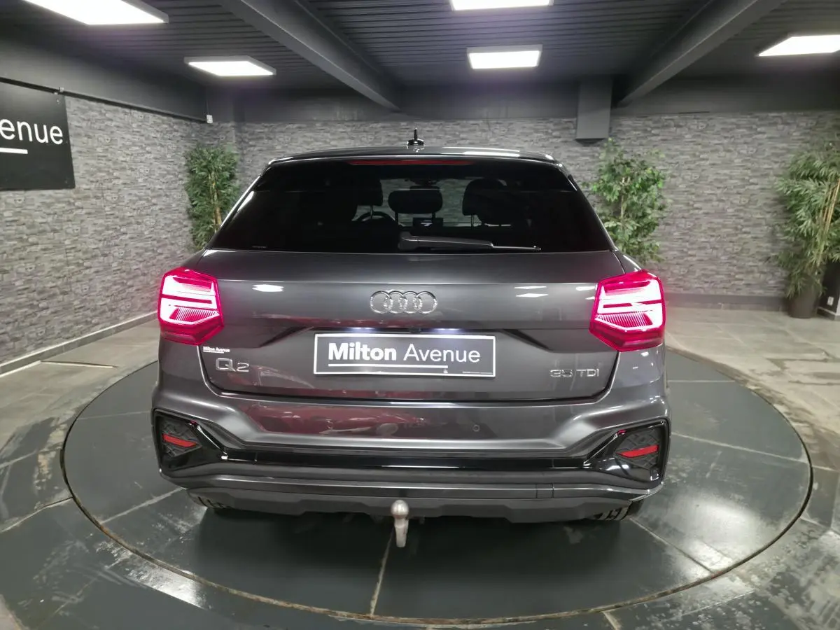 Vue arrière d’un Audi Q2 gris Daytona avec feux LED allumés et attelage amovible en intérieur showroom.