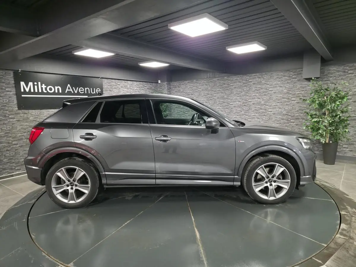 Audi Q2 gris Daytona en vue profil côté gauche, avec jantes alliage 18 pouces et badge S line visible.