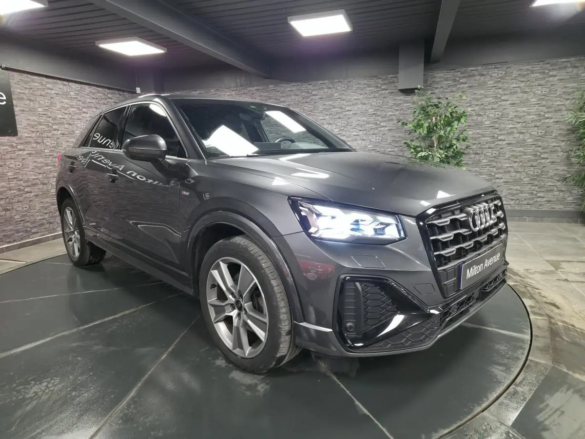 Audi Q2 gris Daytona en 3/4 avant droit avec phares Matrix LED allumés dans un showroom intérieur.