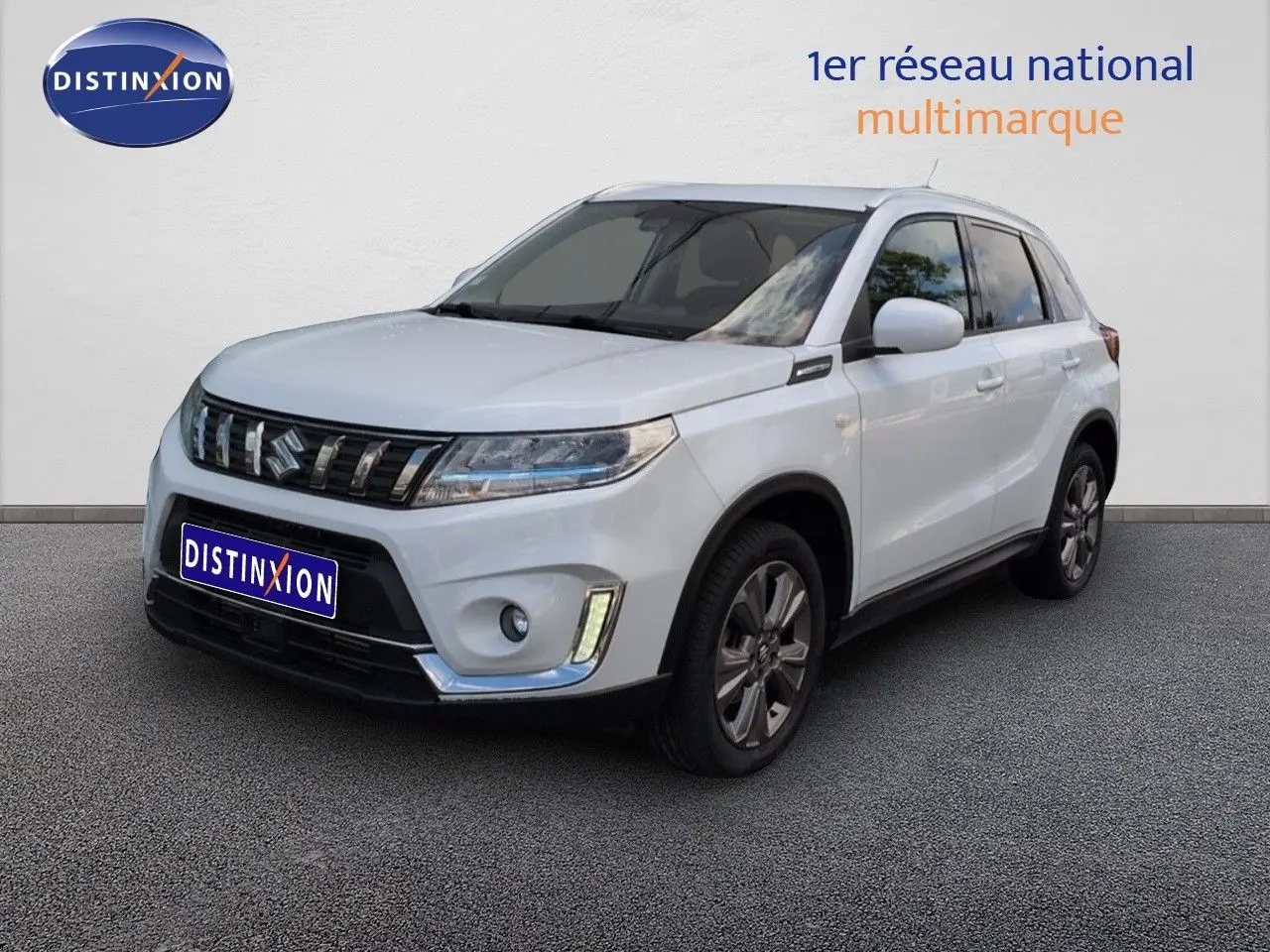 Suzuki Vitara blanc vue 3/4 avant droit, calandre chromée et jantes alliage visibles sur fond neutre.