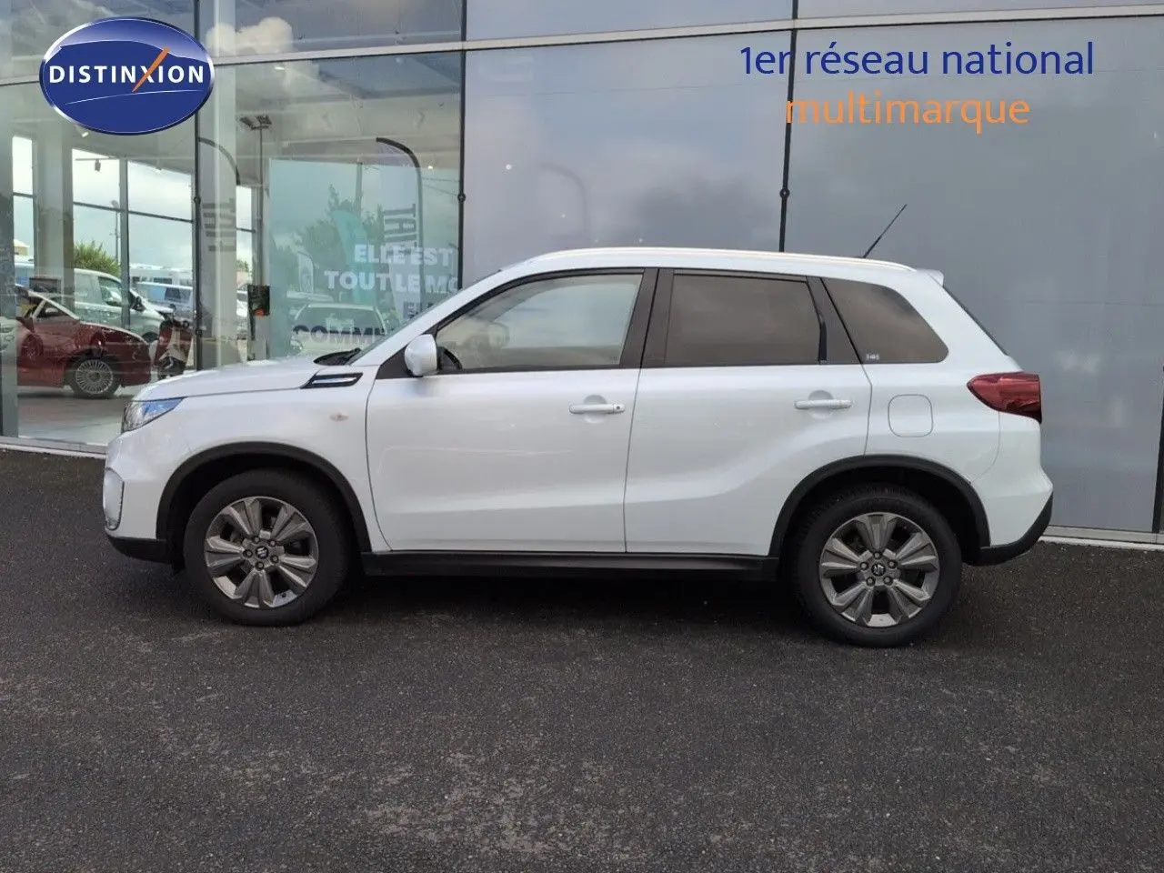 Profil côté gauche d'un Suzuki Vitara blanc avec jantes alu, vitres teintées et lignes de carrosserie marquées.