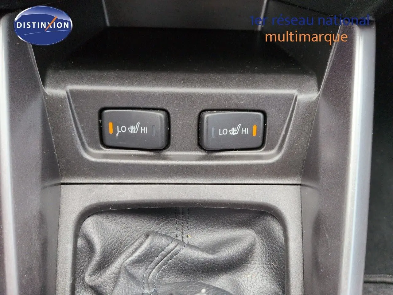 Gros plan sur les commandes des sièges chauffants et soufflet de levier de vitesse en cuir noir dans un Suzuki Vitara gris métallisé.