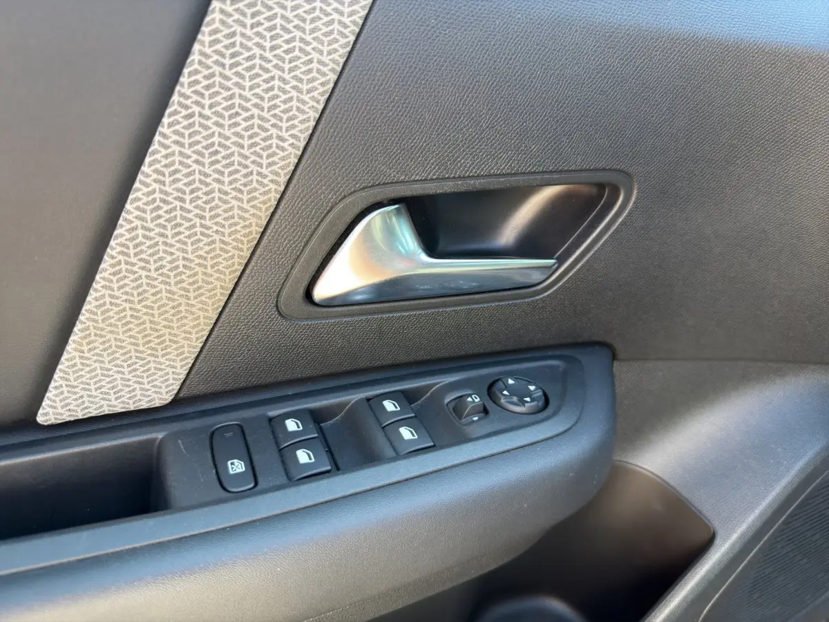 Gros plan sur la poignée intérieure et les commandes de vitres côté conducteur d'une Citroën C4 2023, tissu gris et plastique noir.