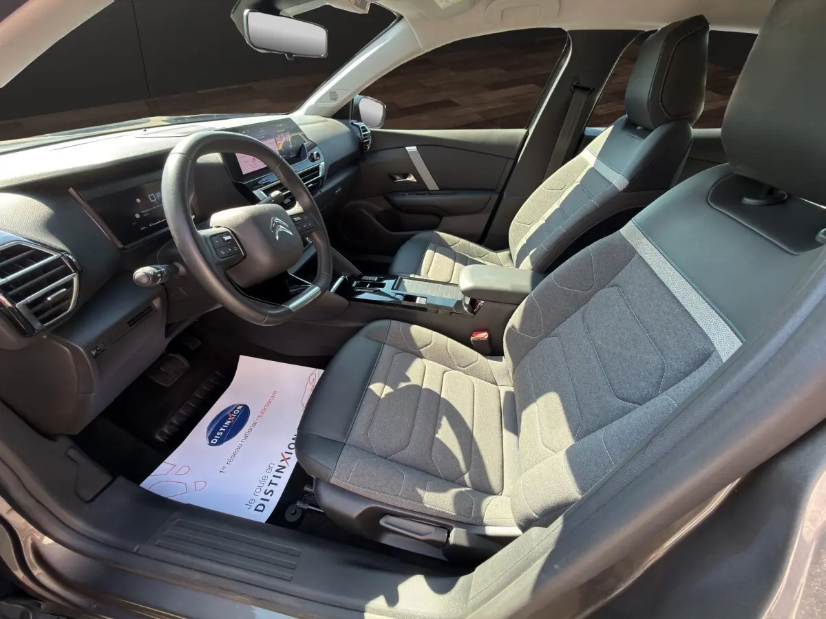 Vue intérieure côté conducteur de la Citroën C4 2023 gris foncé, volant cuir multifonctions et sièges tissu-cuir bicolores.
