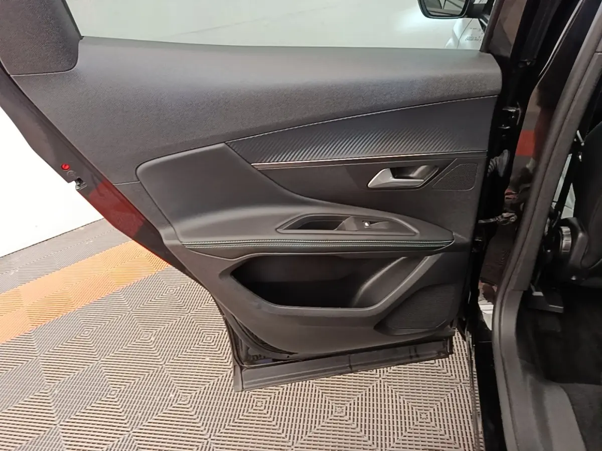 Vue intérieure de la porte arrière droite noire d’un Peugeot 3008, avec garniture tissu et surpiqûres vertes.