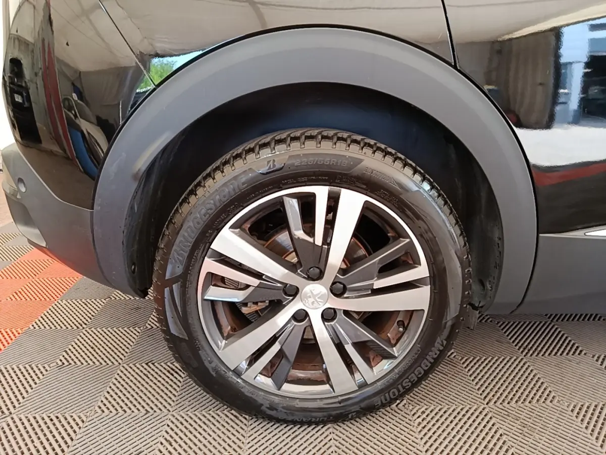 Gros plan sur la roue avant droite d’un Peugeot 3008 noir, mettant en valeur la jante alliage et le pneu Bridgestone.