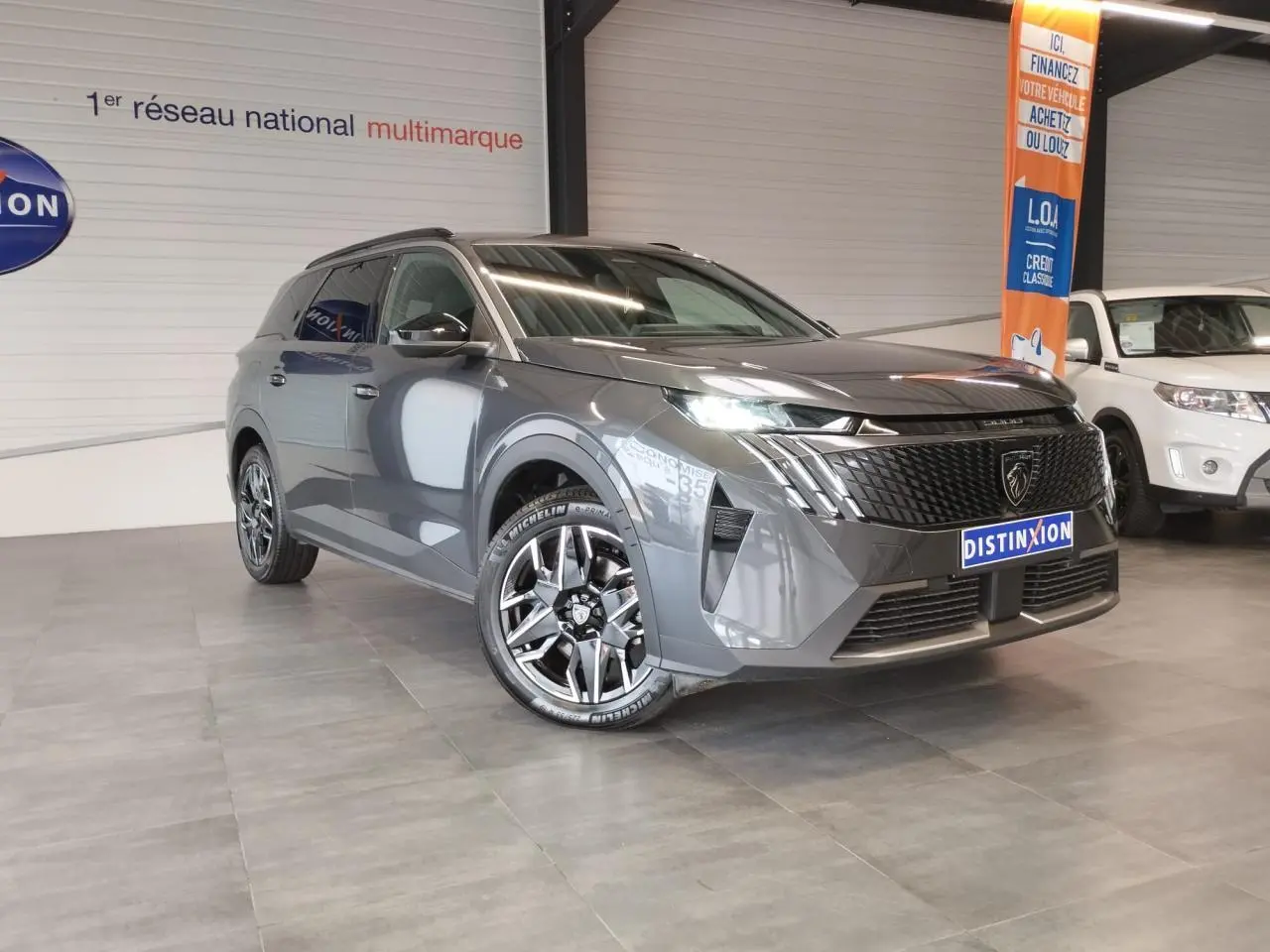 Peugeot 5008 gris titanium en 3/4 avant droit, avec calandre noire et jantes alliage 19 pouces diamantées.