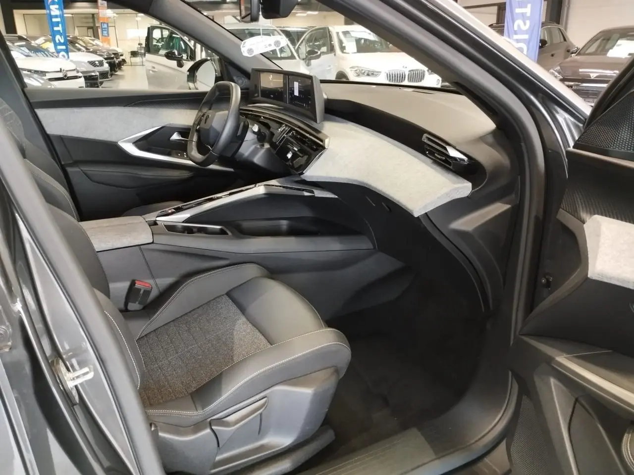 Vue intérieure côté conducteur du Peugeot 5008 2025 gris titanium, avec tableau de bord moderne et sellerie tissu gris et cuir noir.
