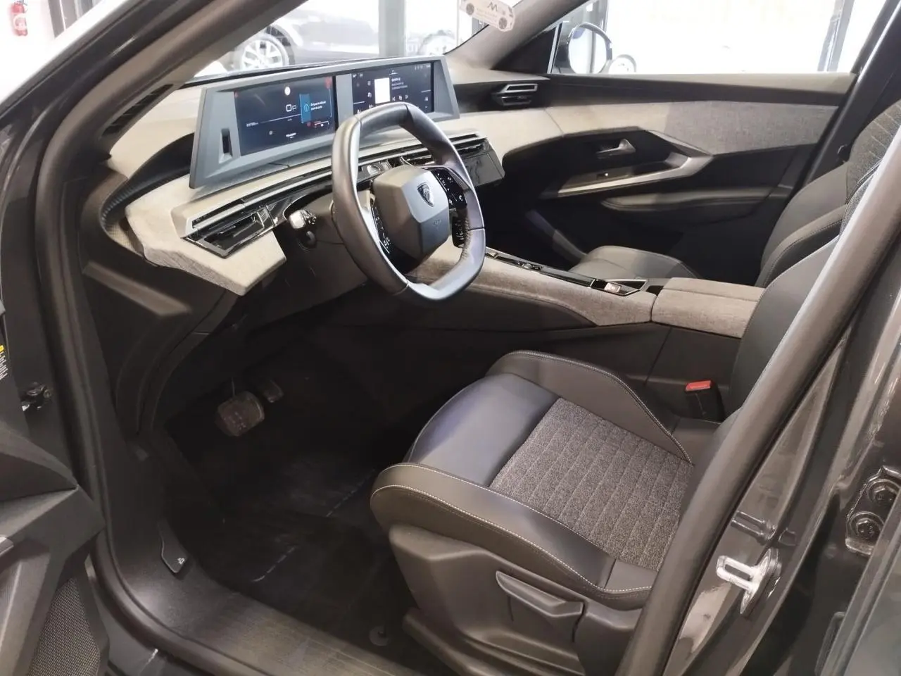 Intérieur avant droit du Peugeot 5008 gris titanium 2025, volant compact et tableau de bord numérique panoramique.