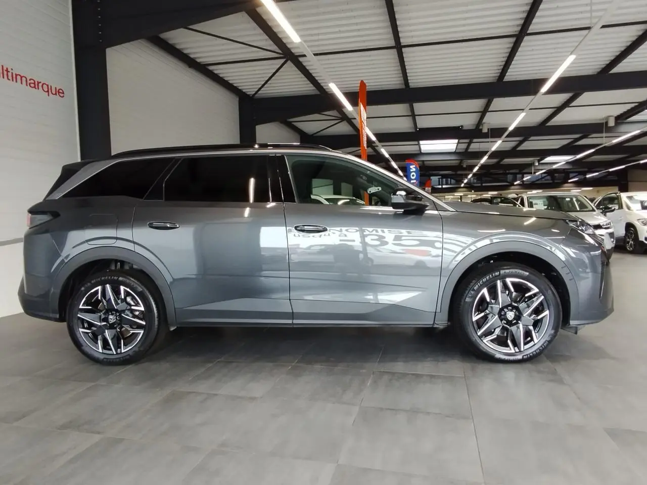 Peugeot 5008 gris titanium vue de profil côté gauche avec jantes alliage 19'' diamantées en intérieur showroom.