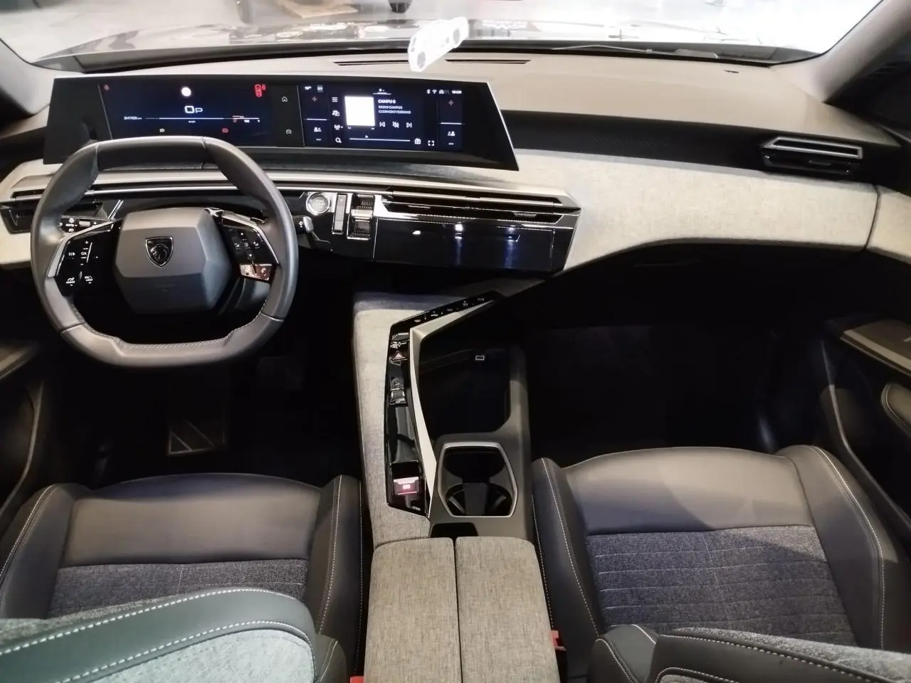 Vue intérieure avant du Peugeot 5008 2025, tableau de bord moderne avec double écran et sellerie tissu gris et cuir noir.