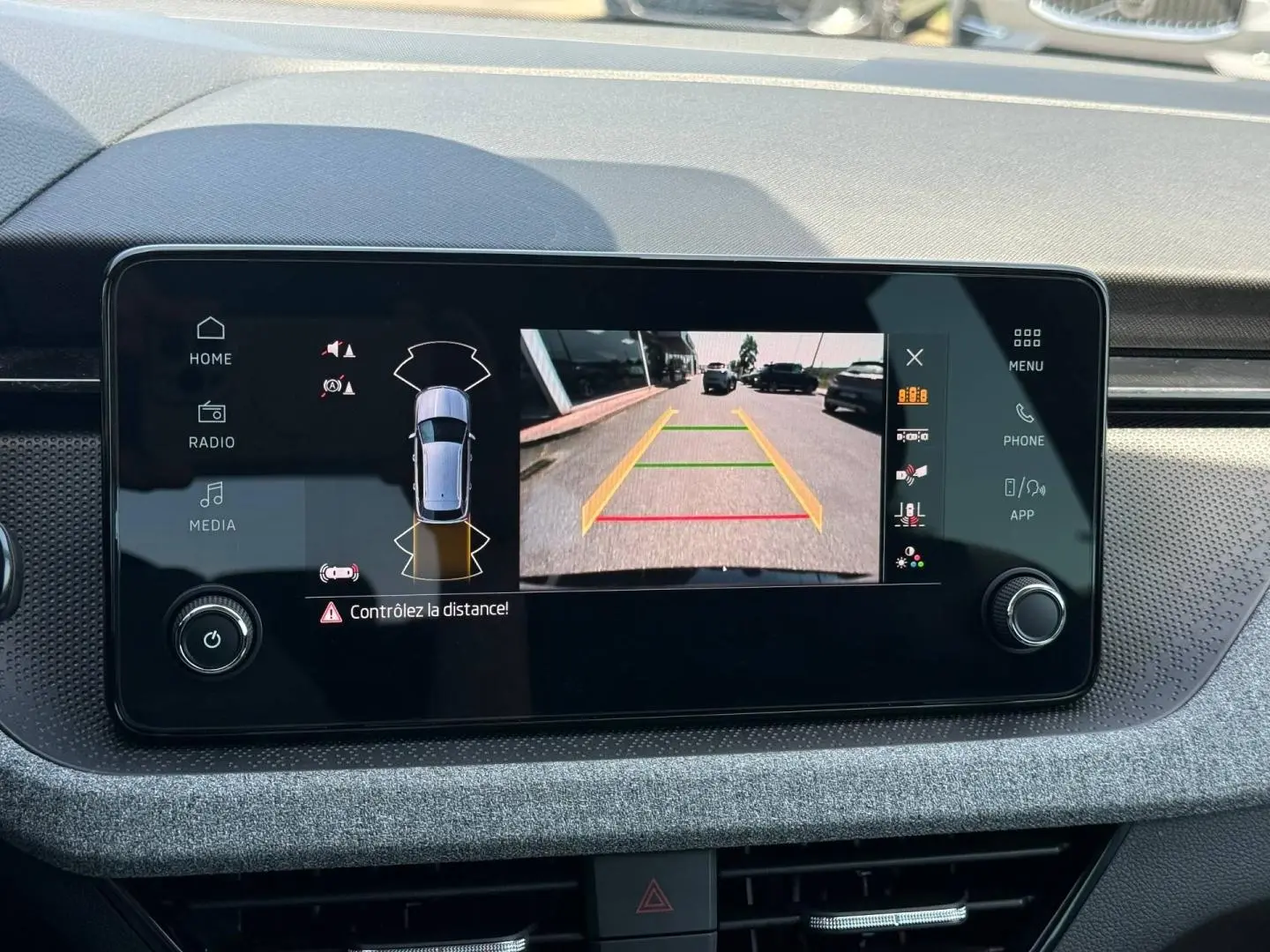 Écran tactile intérieur du Skoda Kamiq 2025 montrant la caméra de recul avec alertes de distance, tableau de bord gris.