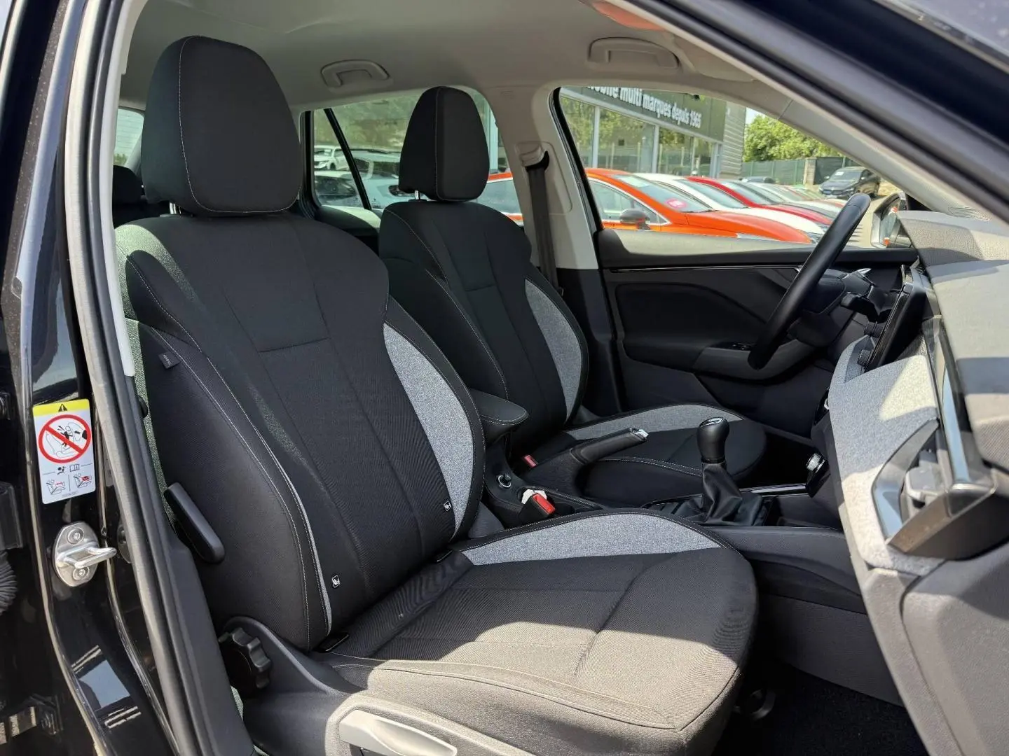 Vue intérieure côté conducteur du Skoda Kamiq 2025 noir Magic nacré, montrant les sièges tissu bicolore et la boîte manuelle.