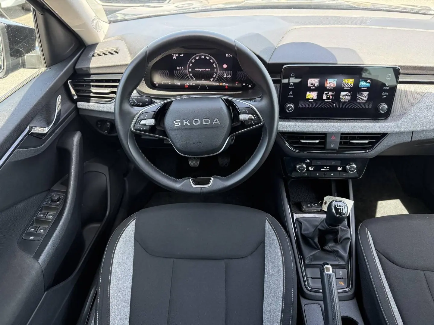 Vue intérieure frontale du Skoda Kamiq 2025, volant multifonction, écran tactile et levier de vitesses manuel visibles.