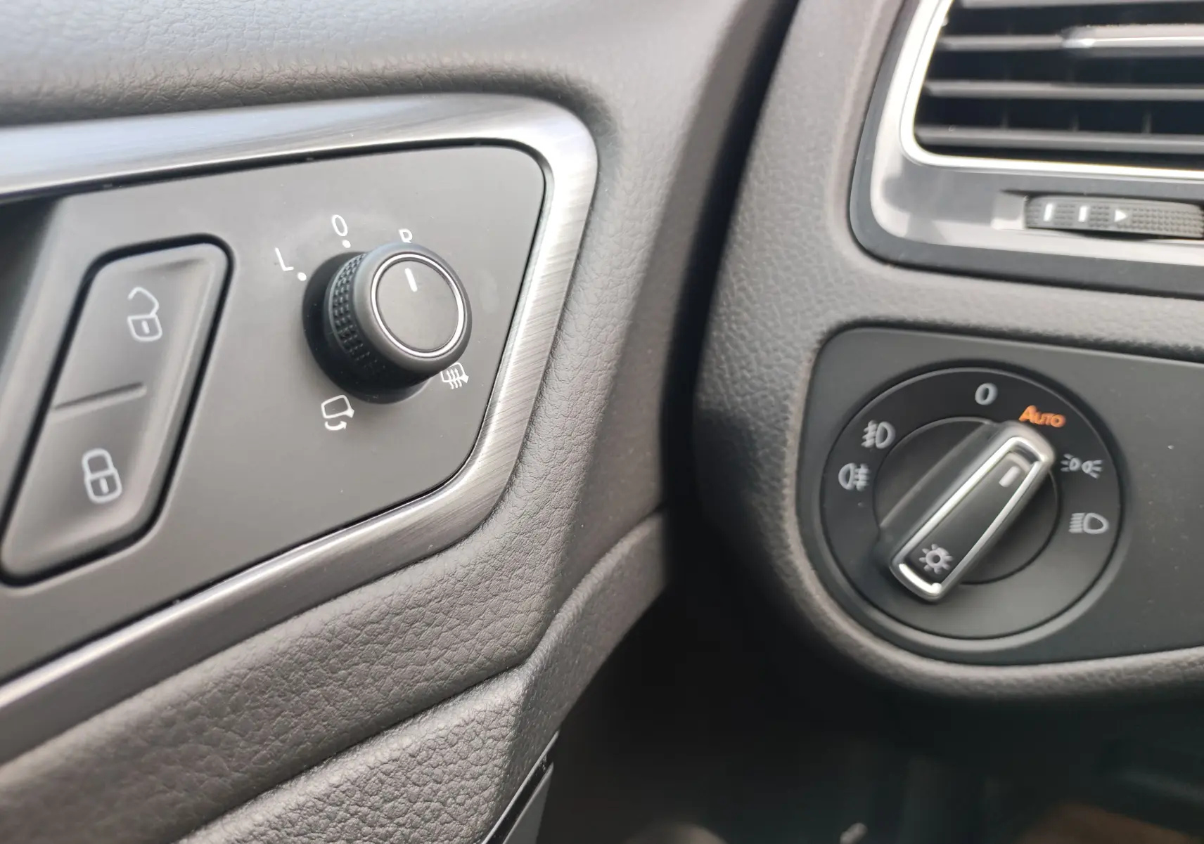 Gros plan sur les commandes d’éclairage et de réglage des rétroviseurs côté gauche dans l’habitacle noir d’une Volkswagen Golf blanche.