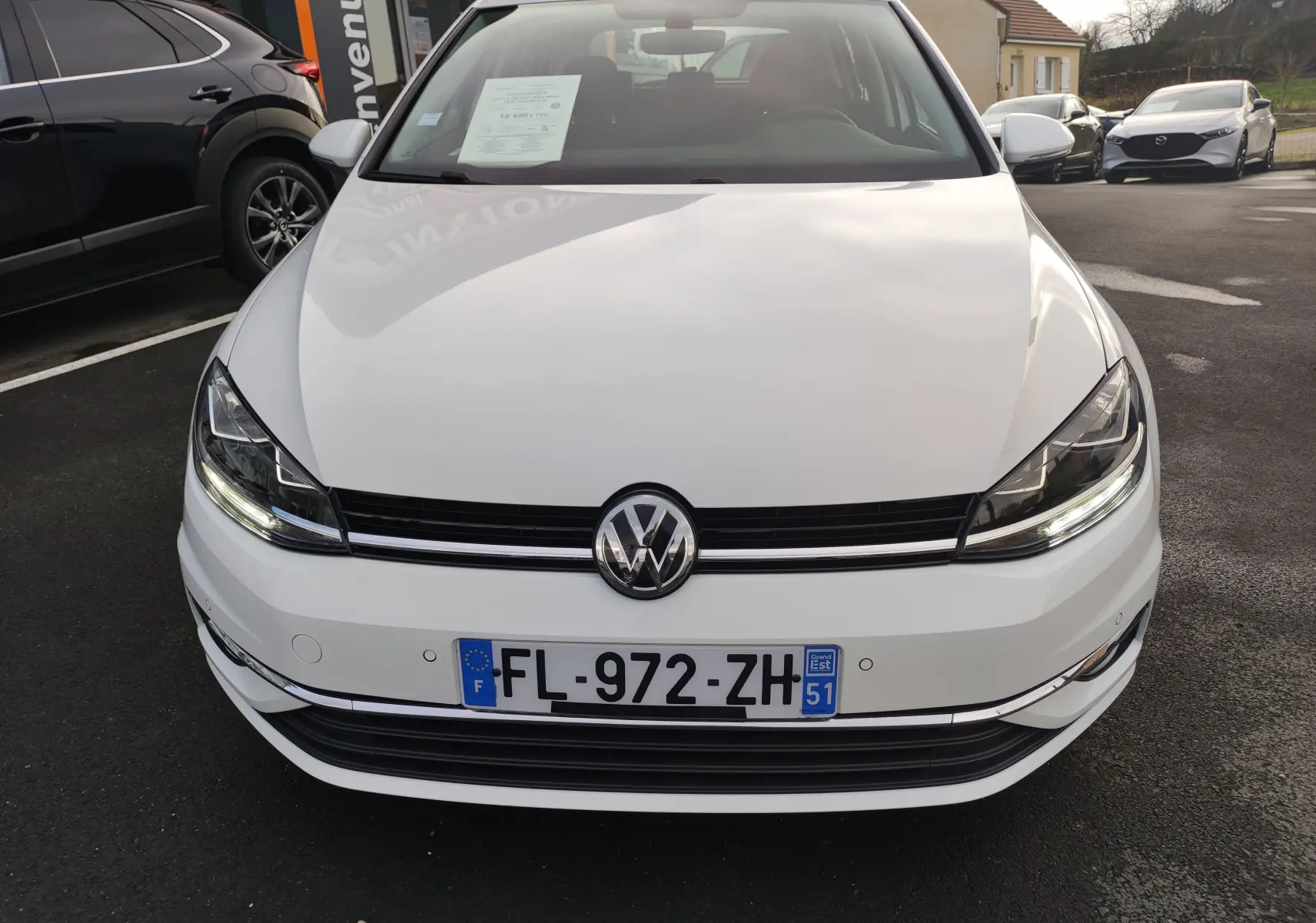 Vue frontale d'une Volkswagen Golf blanche 1.5 TSI EVO 150CV Match de 2019 avec phares LED allumés et plaque d'immatriculation française.