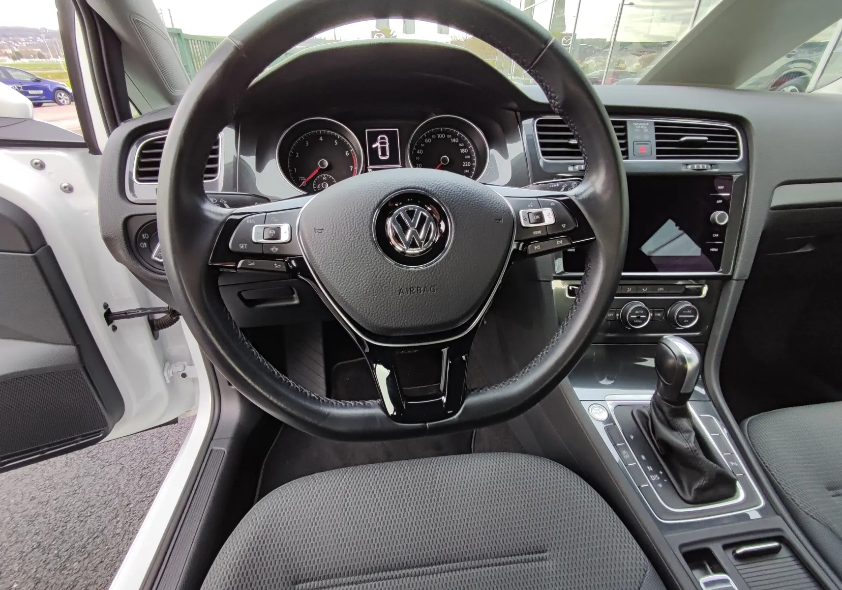 Vue intérieure centrée sur le volant et la console d’une Volkswagen Golf blanche 1.5 TSI EVO 2019 avec boîte auto.