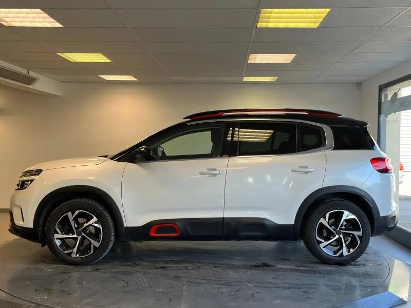 Profil côté gauche du Citroën C5 Aircross blanc nacré avec toit noir et inserts rouges distinctifs sur les bas de caisse.