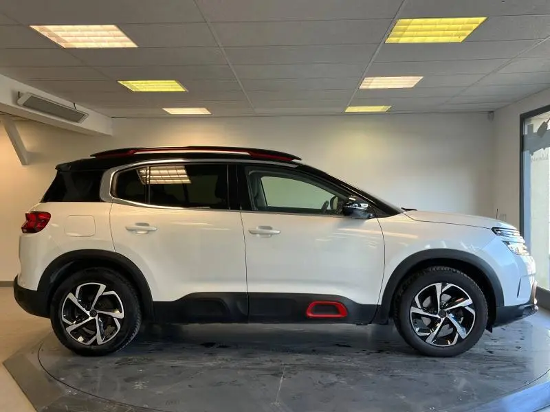 Profil droit d'un Citroën C5 Aircross blanc nacré avec détails rouges et toit noir en intérieur showroom.