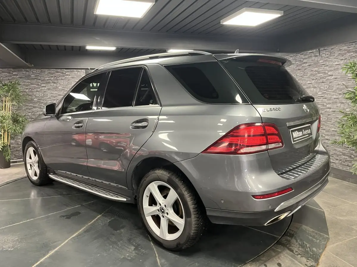 Mercedes GLE gris en vue 3/4 arrière droit, avec vitres teintées foncées et barres de toit chromées visibles.
