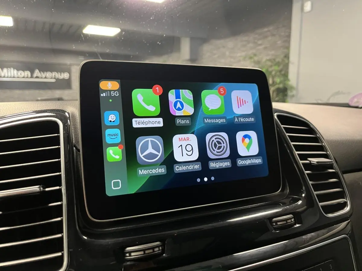 Écran tactile central du Mercedes GLE 2018 affichant Apple CarPlay avec icônes colorées, entouré de grilles d'aération noires.