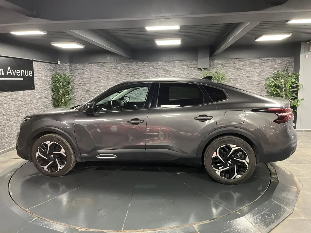 Profil côté gauche d'une Citroën C4 X gris métallisé 2024 avec jantes alliage 18'' Aeroblade en intérieur showroom.