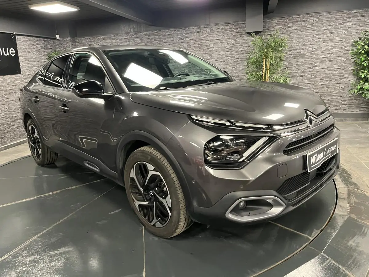 Citroën C4 X gris métallisé vue 3/4 avant droit avec jantes alliage et projecteurs LED en intérieur showroom.