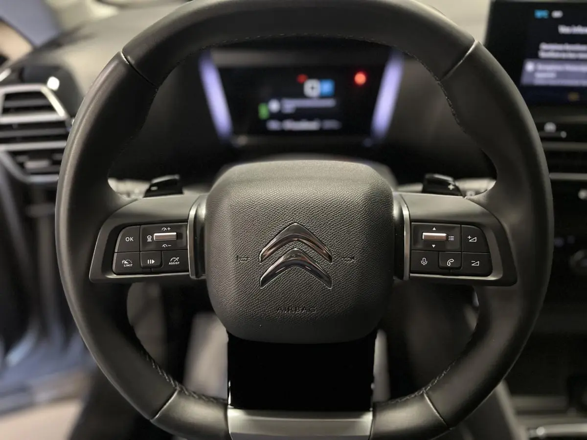 Gros plan sur le volant cuir noir de la Citroën C4 X 2024 avec commandes intégrées et logo chromé central.