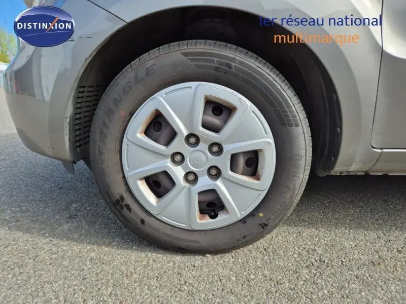 Gros plan sur la roue avant gauche d'une KIA SOUL 2010 gris métallisé avec jante en plastique et logo Kia au centre.