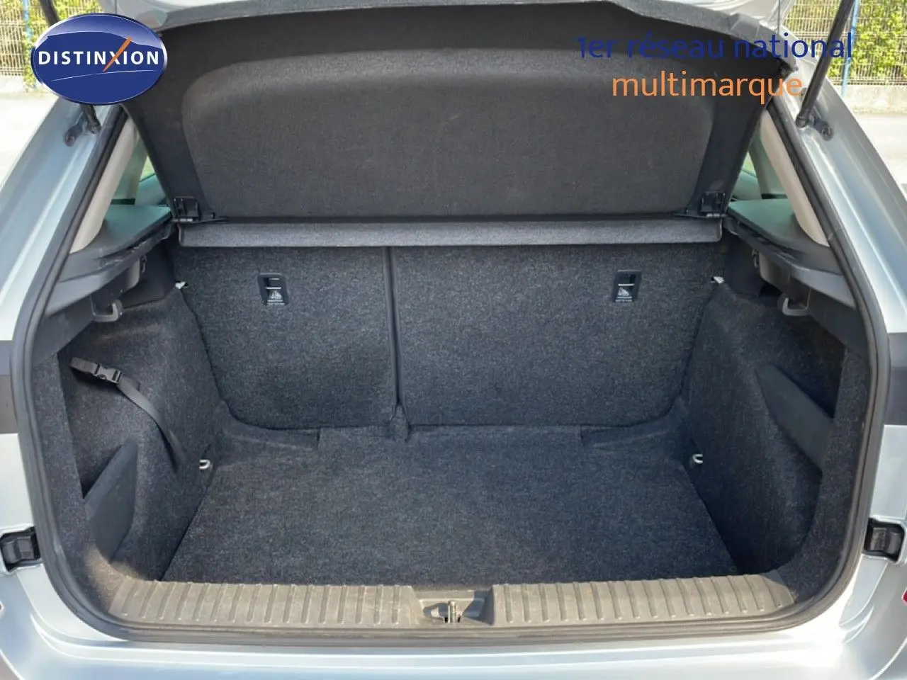 Coffre ouvert vu de l'arrière d'un Skoda Kamiq gris argent métal, montrant l'espace de chargement vide et doublé de tissu gris.