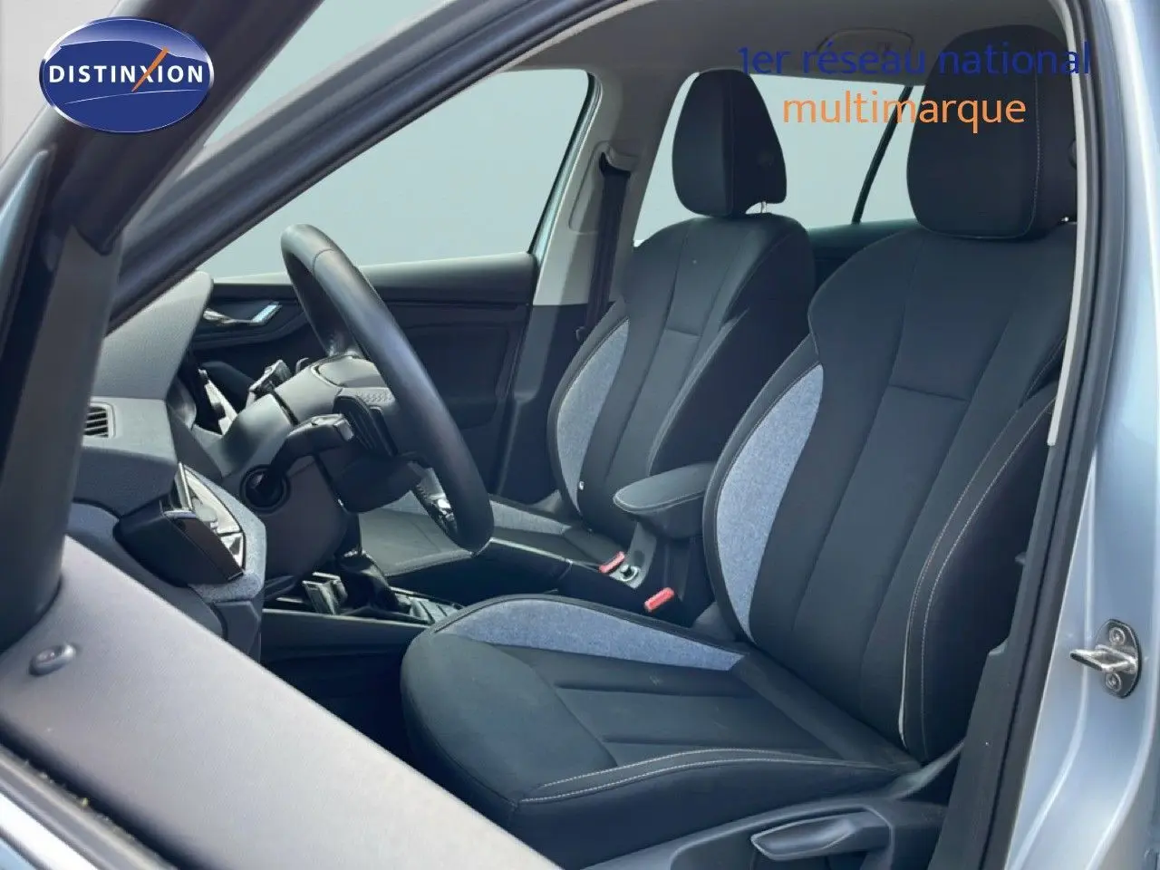 Vue intérieure côté conducteur du Skoda Kamiq gris argent métal 2025, montrant les sièges en tissu noir et gris et le volant multifonction.