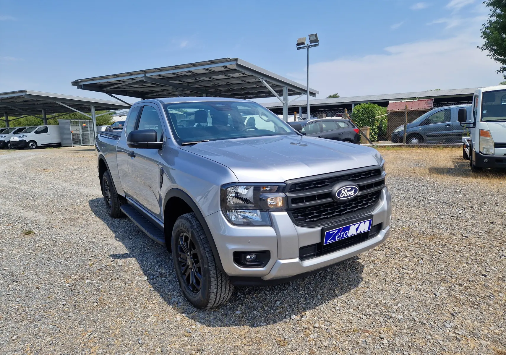Ford Ranger Super Cabine gris Iconic vu en 3/4 avant droit, avec calandre noire et jantes noires sur parking extérieur.