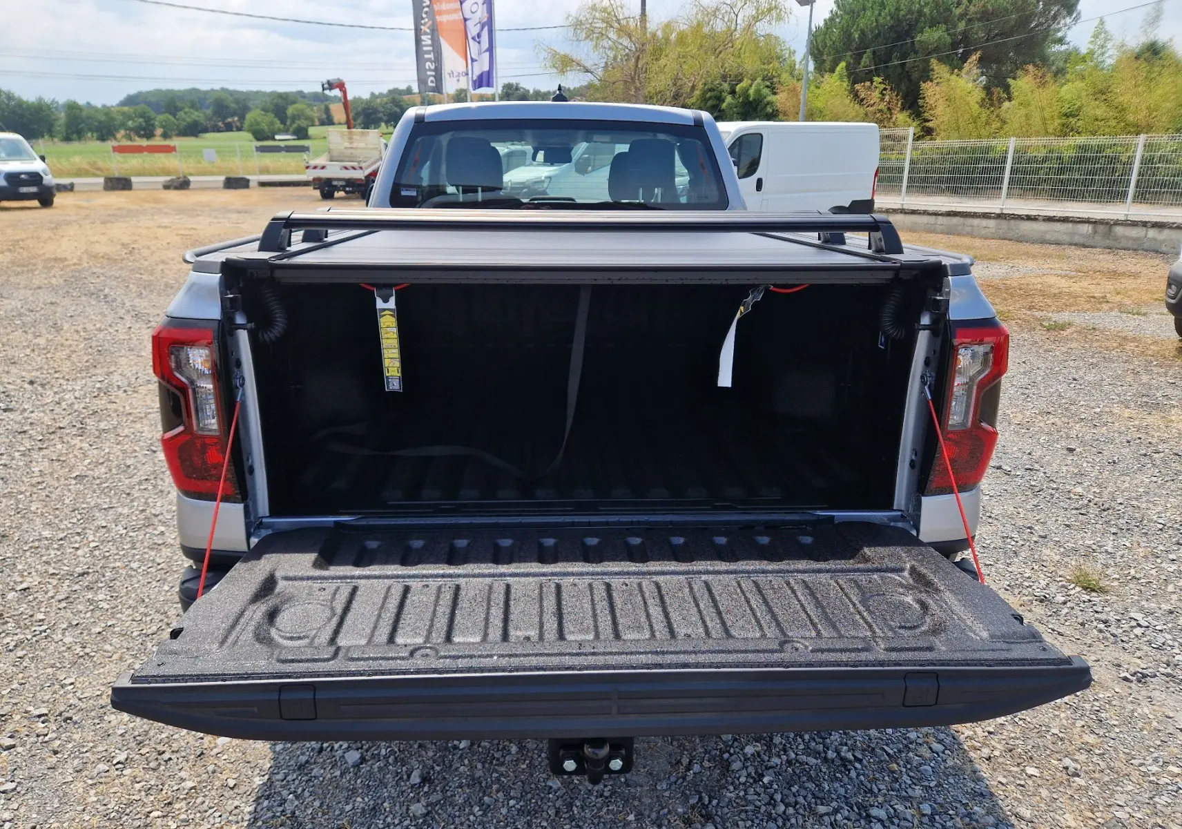 Vue arrière d’un Ford Ranger Super Cabine gris Iconic avec plateau ouvert et rideau rigide coulissant partiellement relevé.