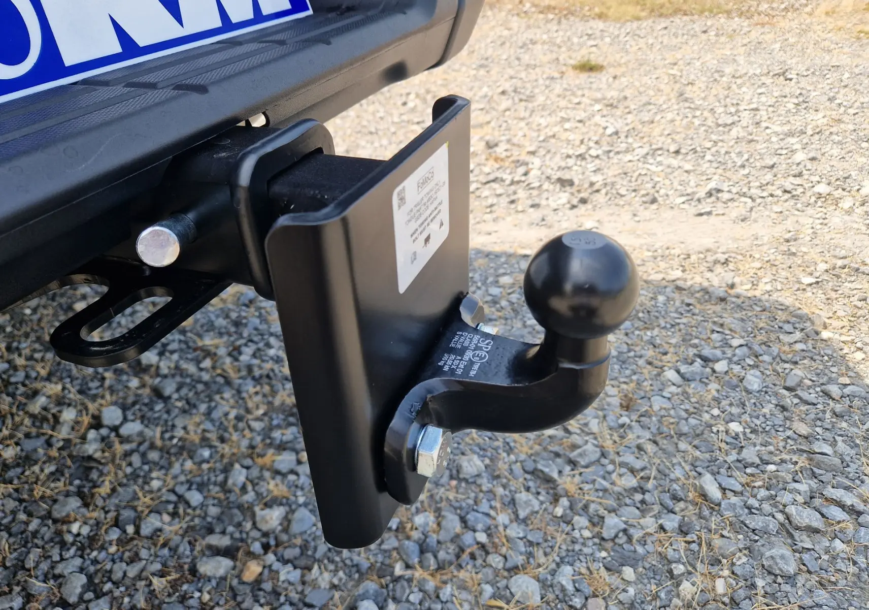 Gros plan sur l'attelage noir fixé à l'arrière du Ford Ranger Super Cabine gris Iconic, posé sur un sol gravillonné.