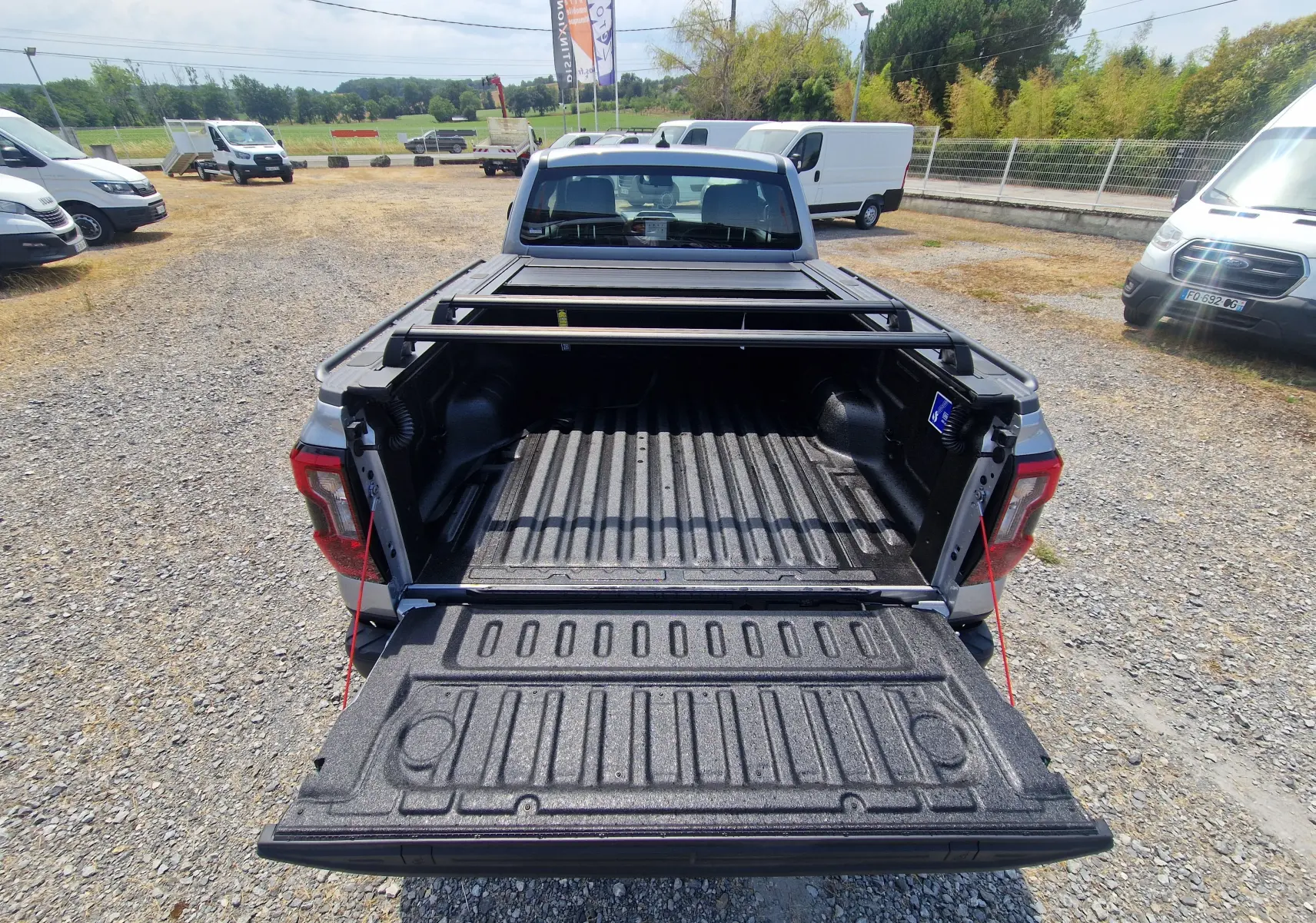 Vue arrière du Ford Ranger Super Cabine gris Iconic avec plateau ouvert, barres de renfort et rideau coulissant manuel visible.