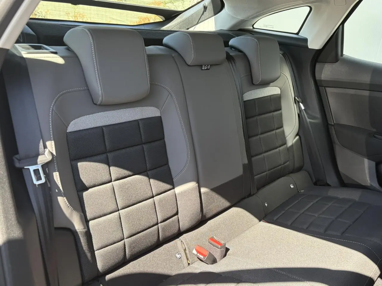 Vue intérieure des sièges arrière gris et noirs de la Citroën C4 Hybrid 2025 avec appuie-têtes et ceintures visibles.