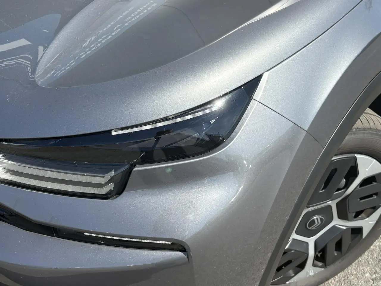 Gros plan sur le phare avant droit et la roue d’une Citroën C4 Hybrid 145 gris Mercury avec détails lumineux modernes.