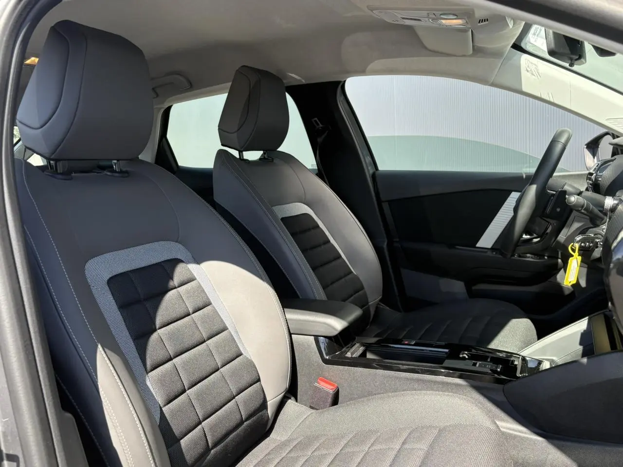 Intérieur avant de la Citroën C4 Hybrid 2025, vue côté droit, sièges tissu noir et gris avec accoudoir central.