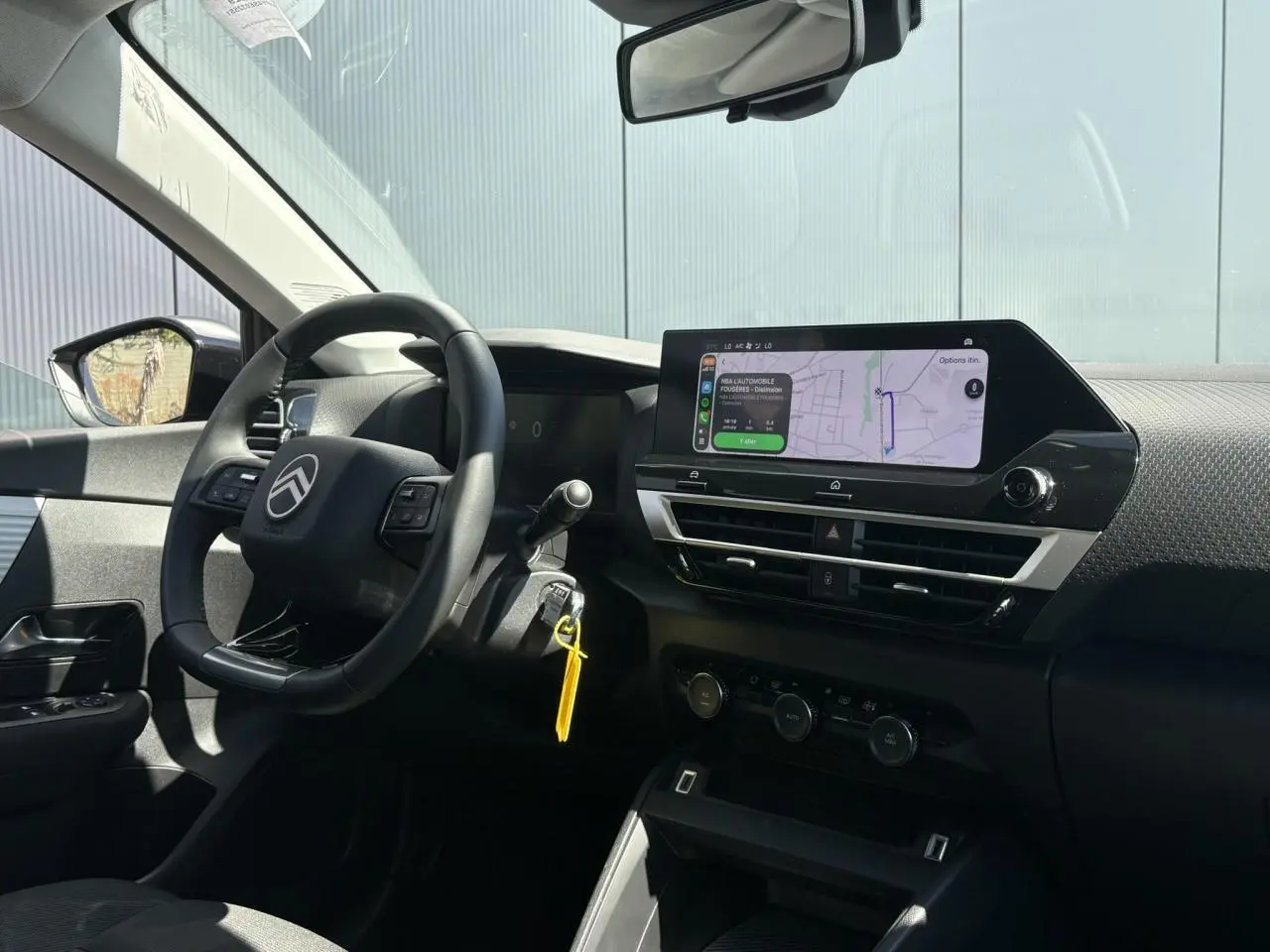 Intérieur de la Citroën C4 Hybrid 2025 vu côté conducteur, tableau de bord noir avec écran tactile de navigation allumé.