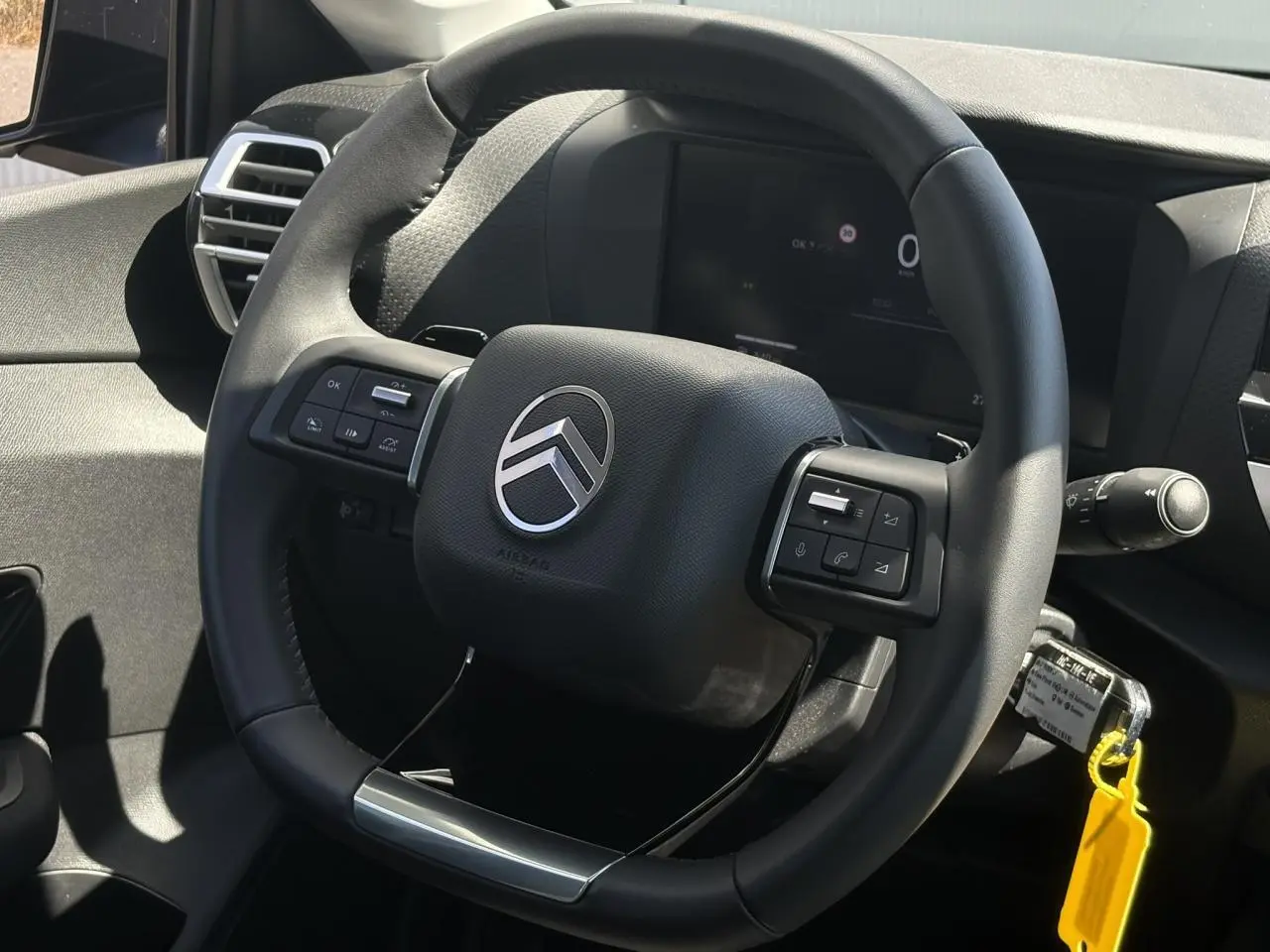 Gros plan sur le volant cuir noir de la Citroën C4 Hybrid 2025, avec commandes intégrées et tableau de bord numérique en arrière-plan.