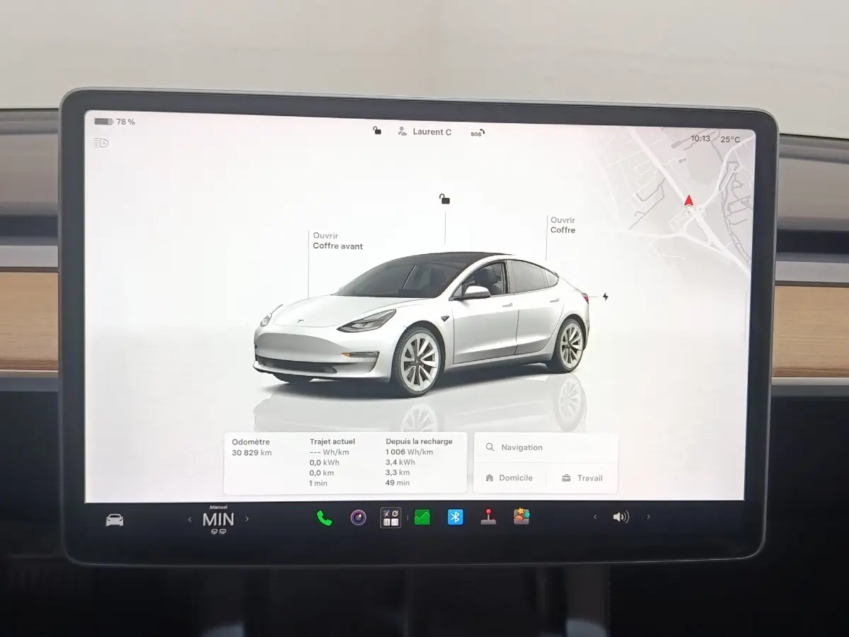 Écran tactile central montrant une Tesla Model 3 blanche en 3/4 avant droit avec interface de contrôle et navigation.