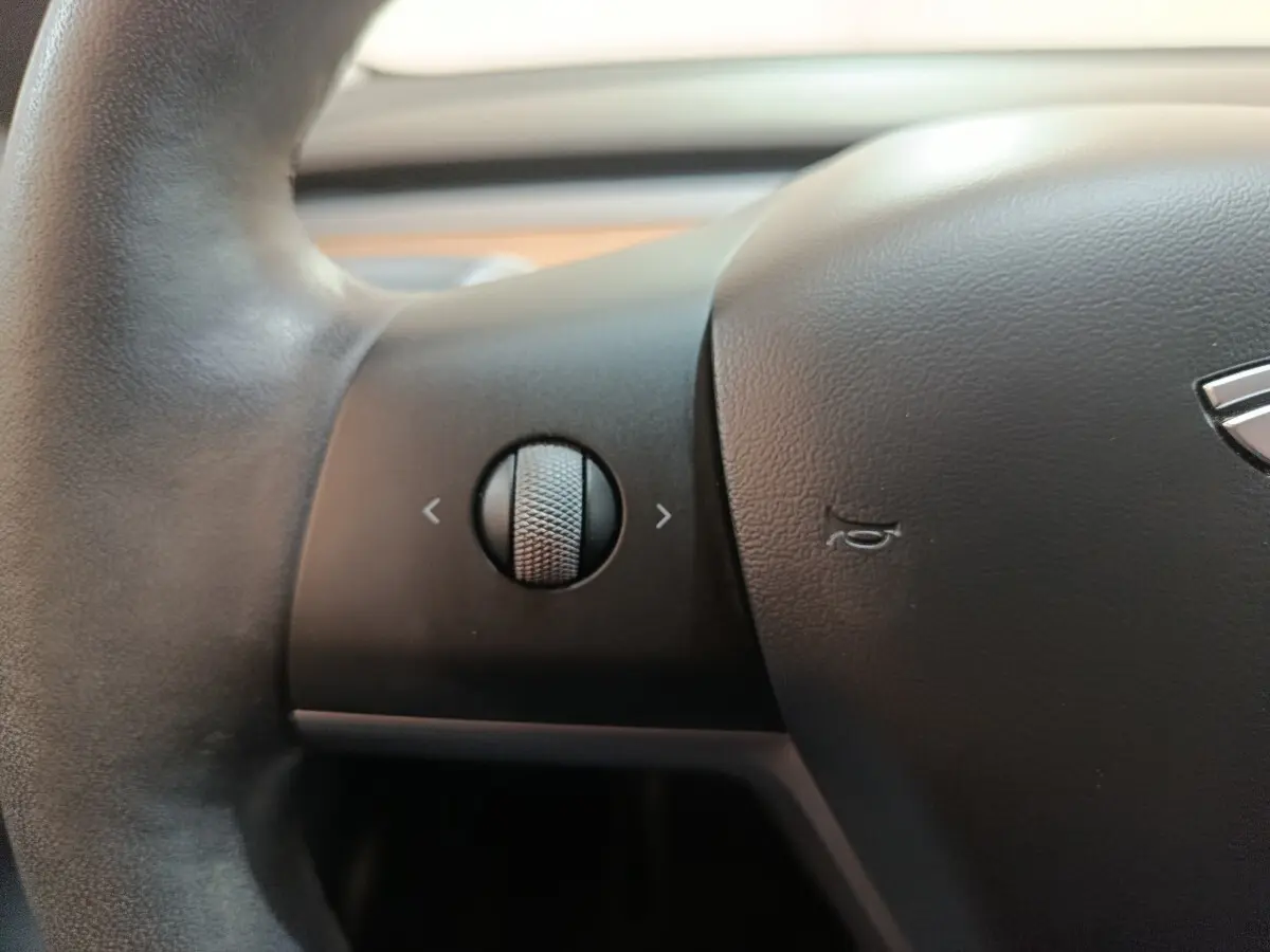Gros plan sur le volant noir de la Tesla Model 3 2022 avec molette de commande et logo partiel visible.