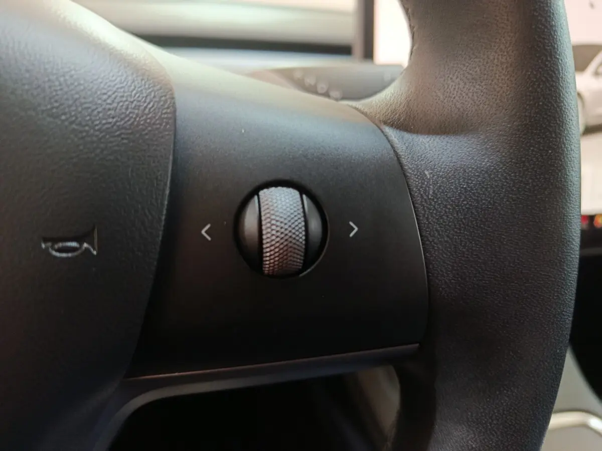 Gros plan sur la molette de commande noire du volant en cuir synthétique d'une Tesla Model 3 blanche de 2022.
