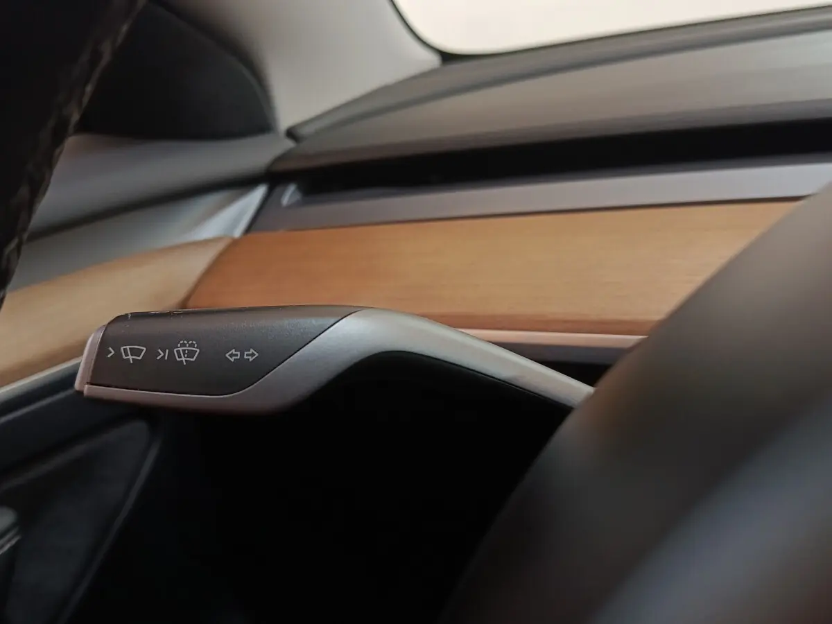 Détail intérieur du levier de clignotant et essuie-glace dans une Tesla Model 3 2022 avec tableau de bord en bois clair.