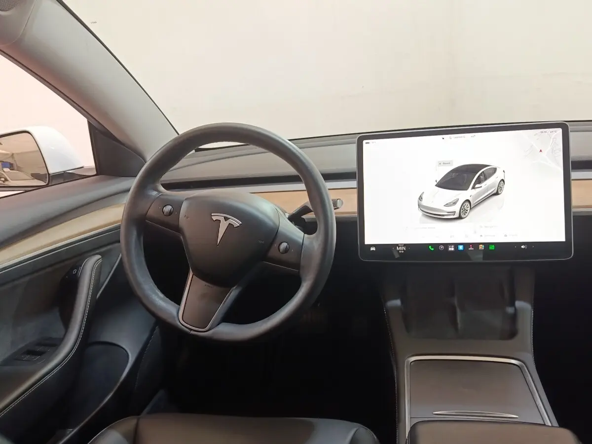 Intérieur Tesla Model 3 blanc 2022, vue du poste de conduite avec volant multifonctions et grand écran tactile central.