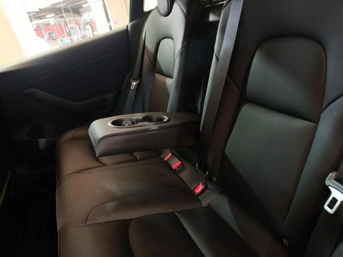 Vue intérieure montrant la banquette arrière noire avec accoudoir central et porte-gobelets dans une Tesla Model 3 Grande Autonomie.