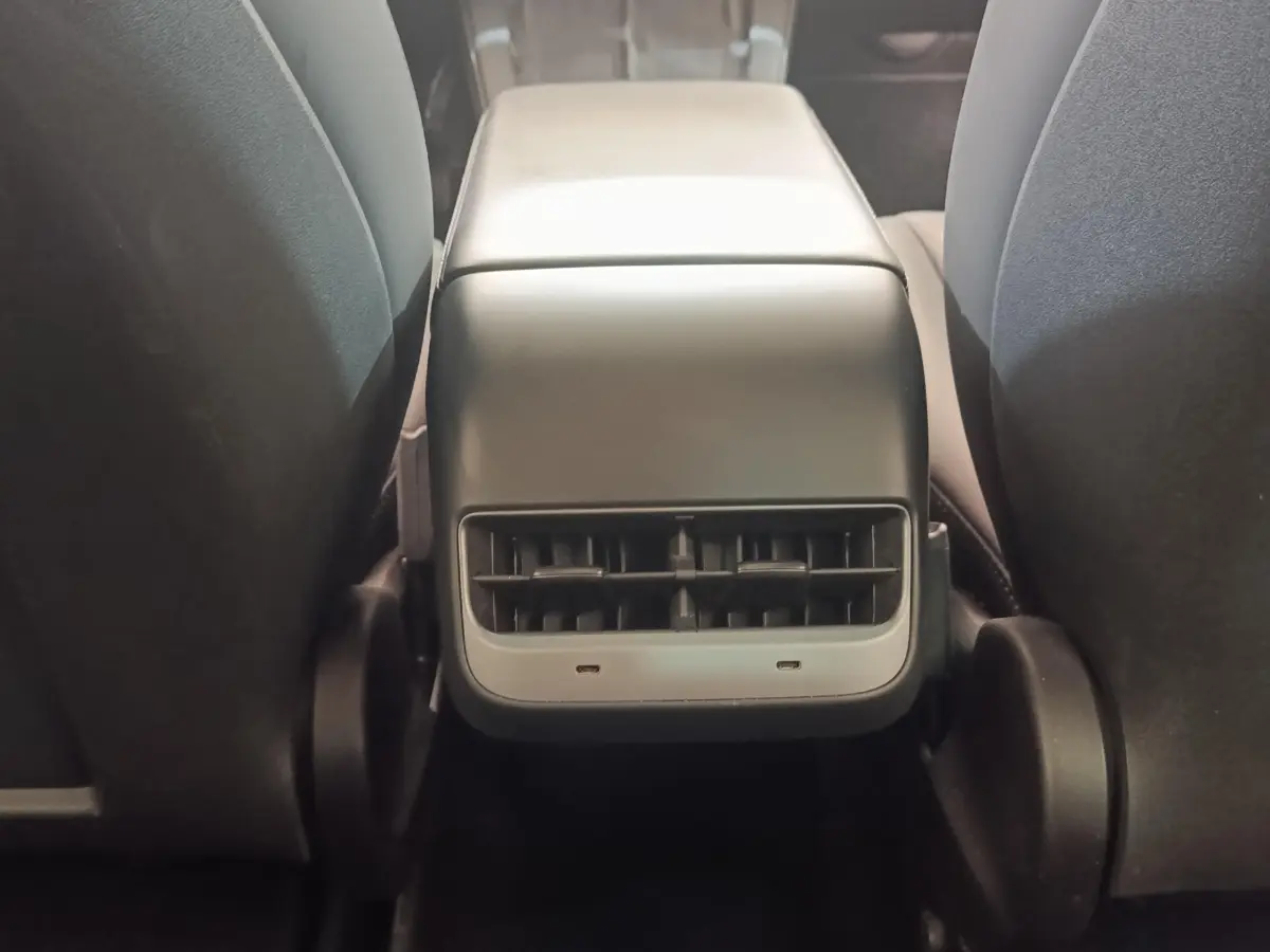 Vue rapprochée de la console centrale arrière noire entre les sièges avant d'une Tesla Model 3 blanche.