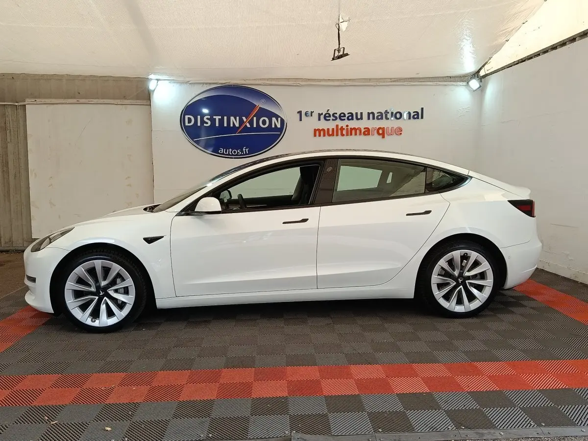 Profil latéral gauche d'une Tesla Model 3 blanche 2022, avec jantes distinctives et poignées affleurantes.